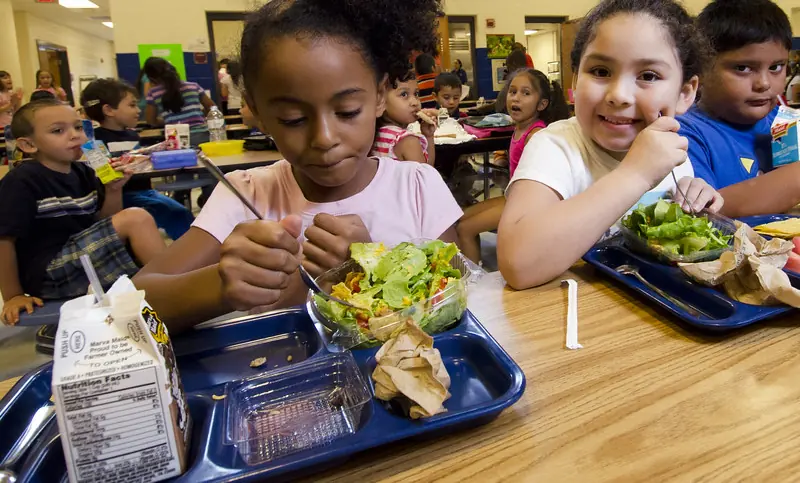 Children eating salad and lunch together in a school cafeteria