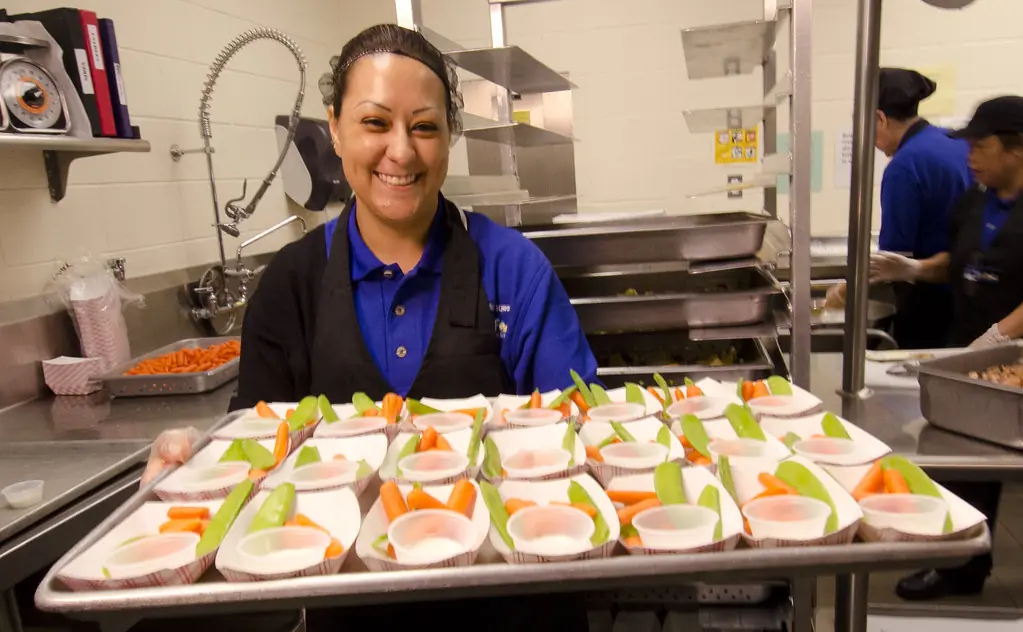 A smiling lunch server holding a tray of prepared vegetable cups